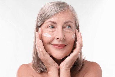 Senior woman with face cream on white background