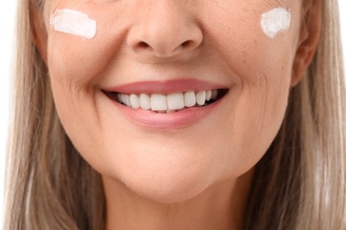 Photo of Senior woman with face cream on white background, closeup