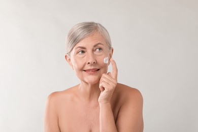 Senior woman applying face cream on light background