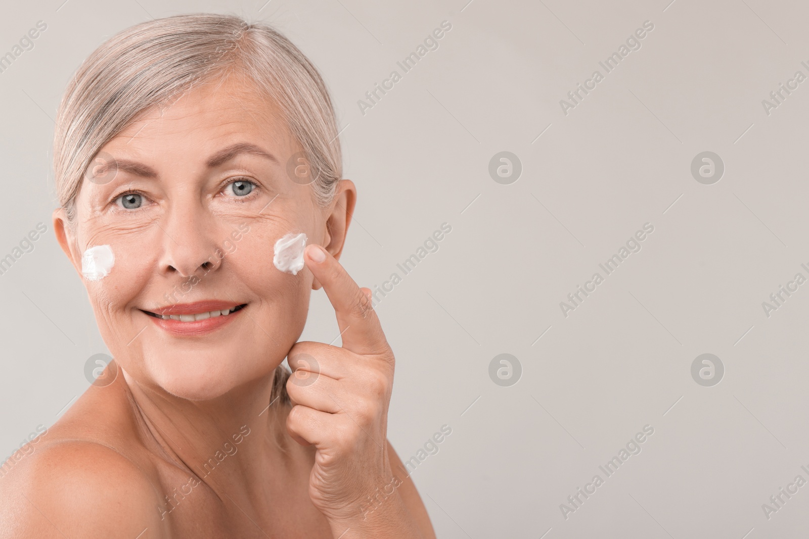 Photo of Senior woman applying face cream on light background. Space for text