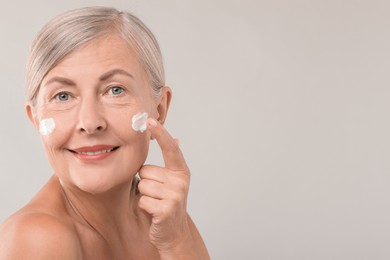 Photo of Senior woman applying face cream on light background. Space for text