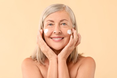 Photo of Senior woman with face cream on beige background