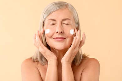 Photo of Senior woman with face cream on beige background