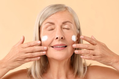 Photo of Senior woman with face cream on beige background