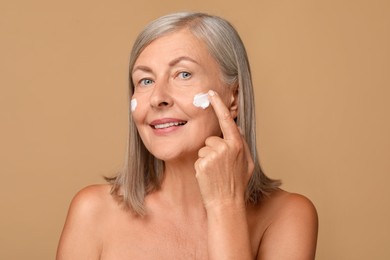 Senior woman applying face cream on beige background