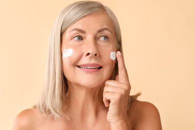 Photo of Senior woman applying face cream on beige background