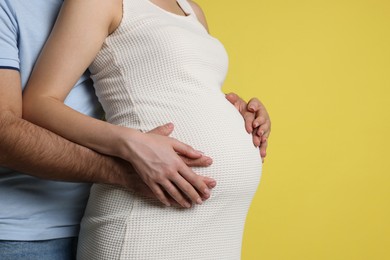 Photo of Man hugging her pregnant wife on yellow background, closeup. Space for text