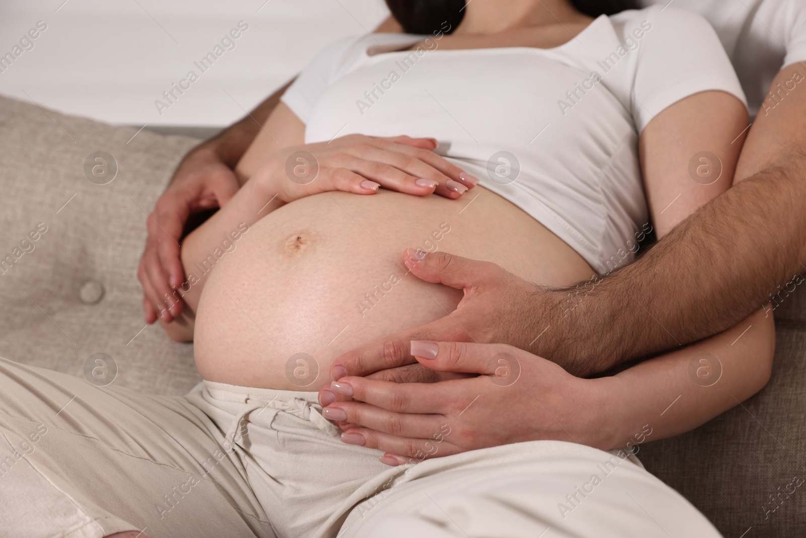 Photo of Man touching his pregnant wife's belly indoors, closeup