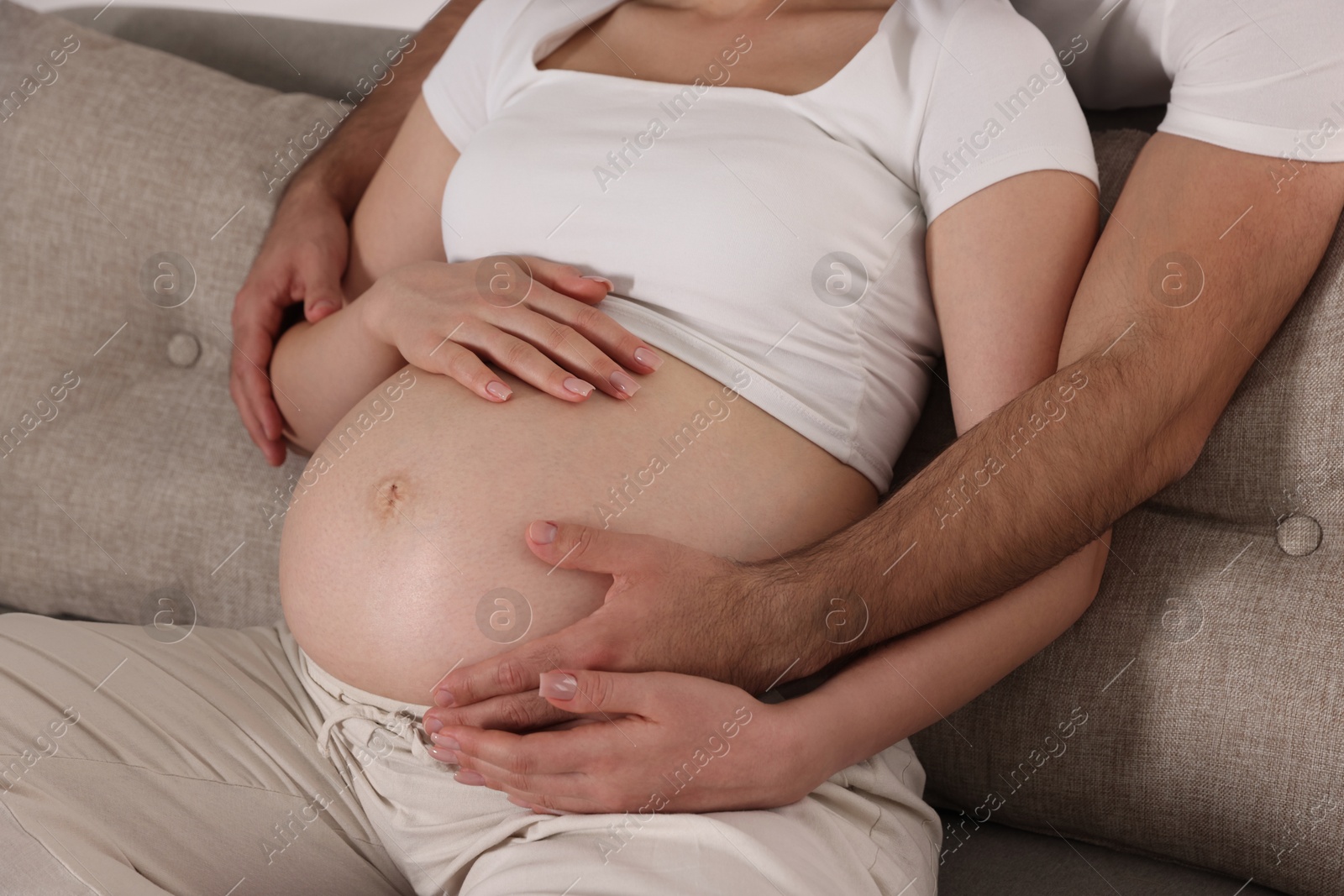 Photo of Man touching his pregnant wife's belly indoors, closeup