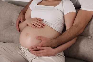 Photo of Man touching his pregnant wife's belly indoors, closeup