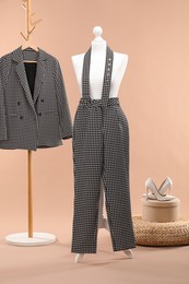 Photo of One female mannequin with pants, pouf, shoes and rack with jacket against beige background