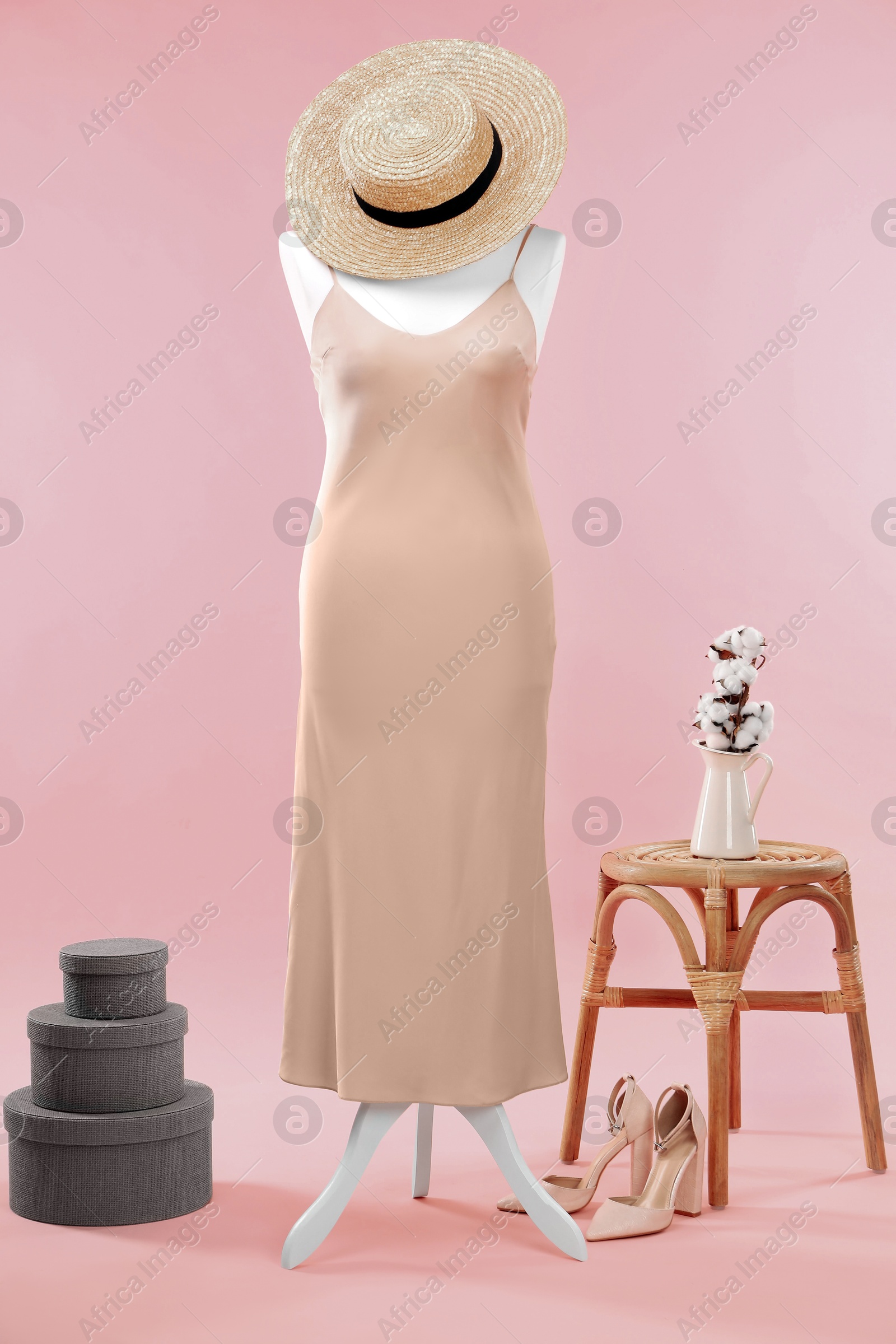 Photo of Female mannequin with dress, hat, shoes, boxes, stool and cotton flowers on pink background