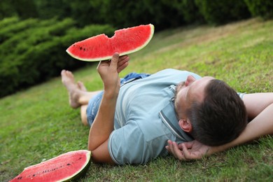 Photo of Happy man with slice of juicy watermelon on green grass outdoors