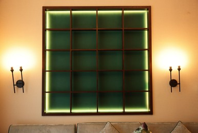 Empty illuminated wooden shelving unit and lamps on beige wall in hotel room