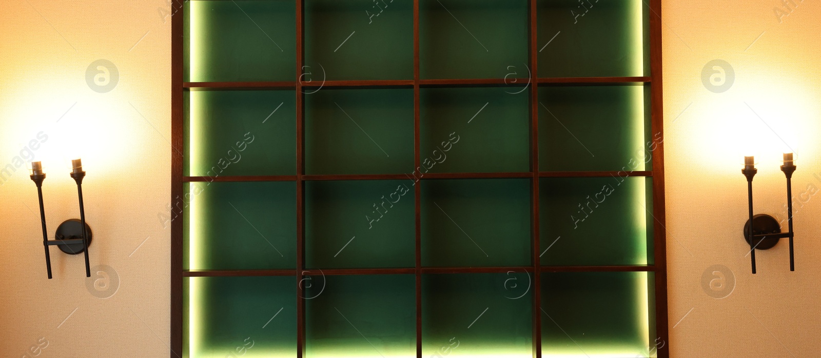 Photo of Empty illuminated wooden shelving unit and lamps on beige wall in hotel room