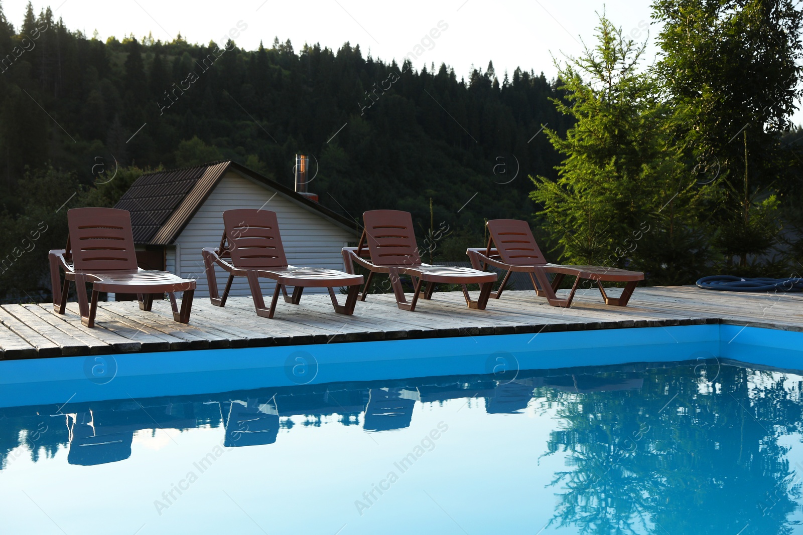 Photo of Outdoor swimming pool, sunbeds and house near forest