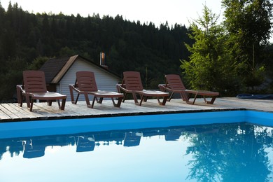 Photo of Outdoor swimming pool, sunbeds and house near forest