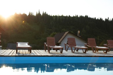 Photo of Outdoor swimming pool, sunbeds and house near forest on sunny day