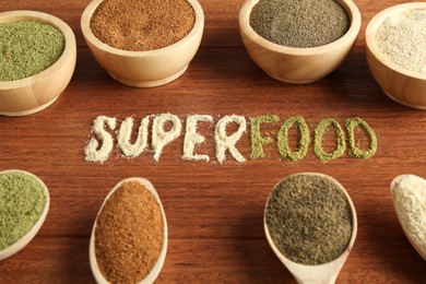 Photo of Word Superfood and different healthy powders on wooden table, closeup