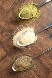 Different superfood powders in spoons on wooden table, flat lay