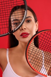 Portrait of beautiful young woman with tennis rackets on red background