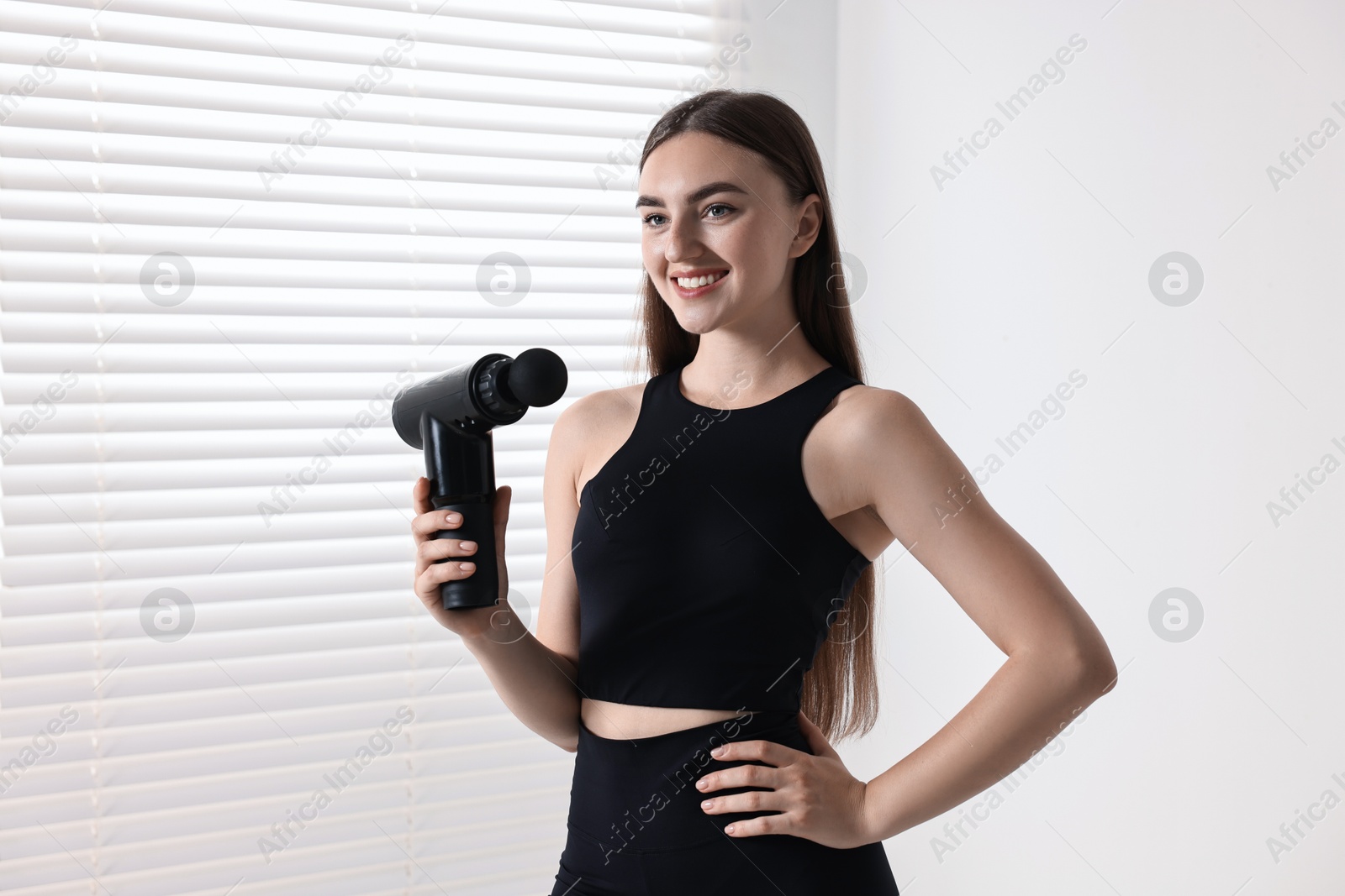 Photo of Young woman with percussive massage gun indoors