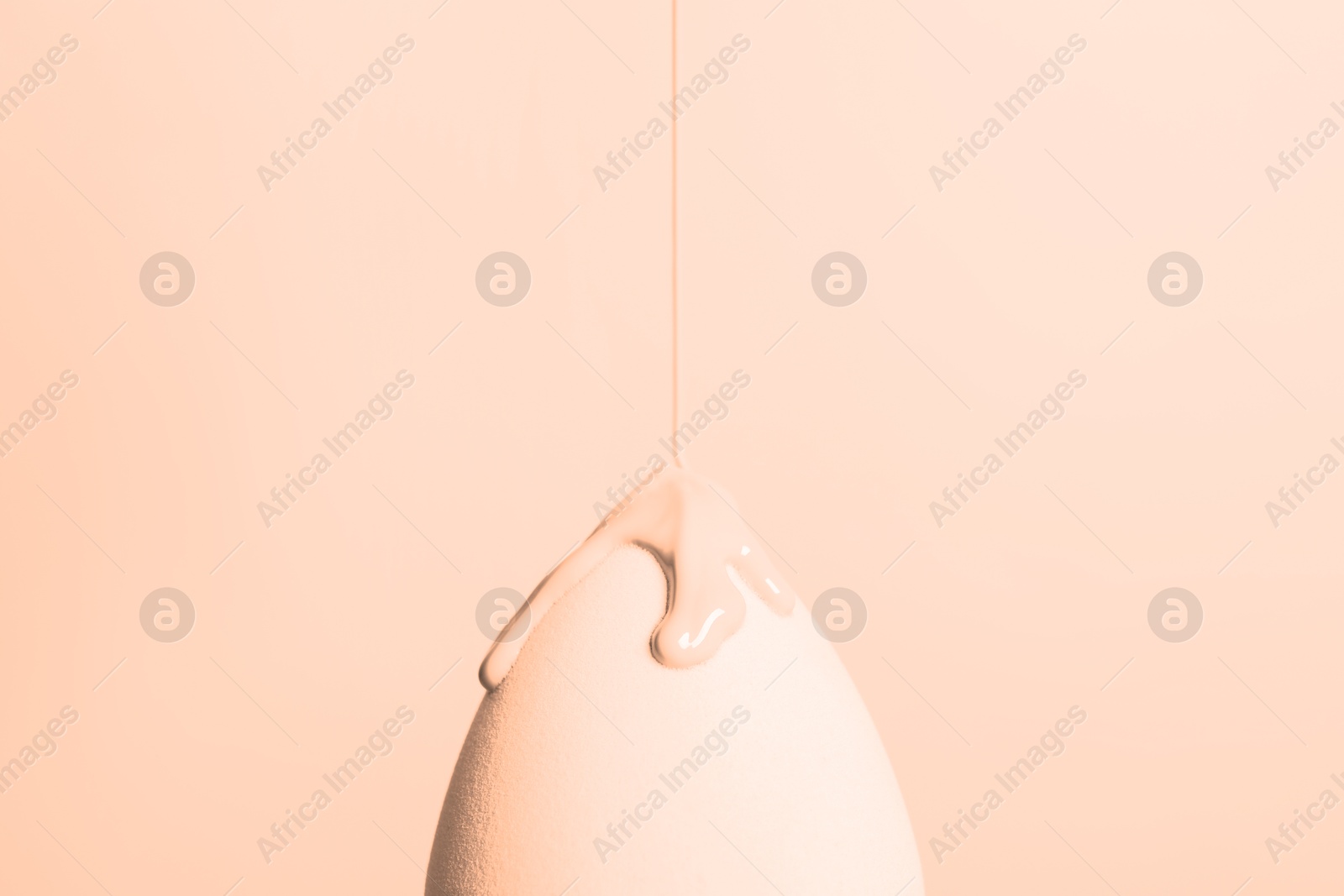 Image of Pouring skin foundation onto makeup sponge on beige background, closeup