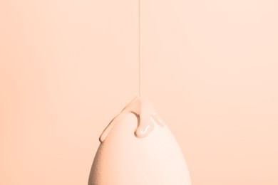 Image of Pouring skin foundation onto makeup sponge on beige background, closeup