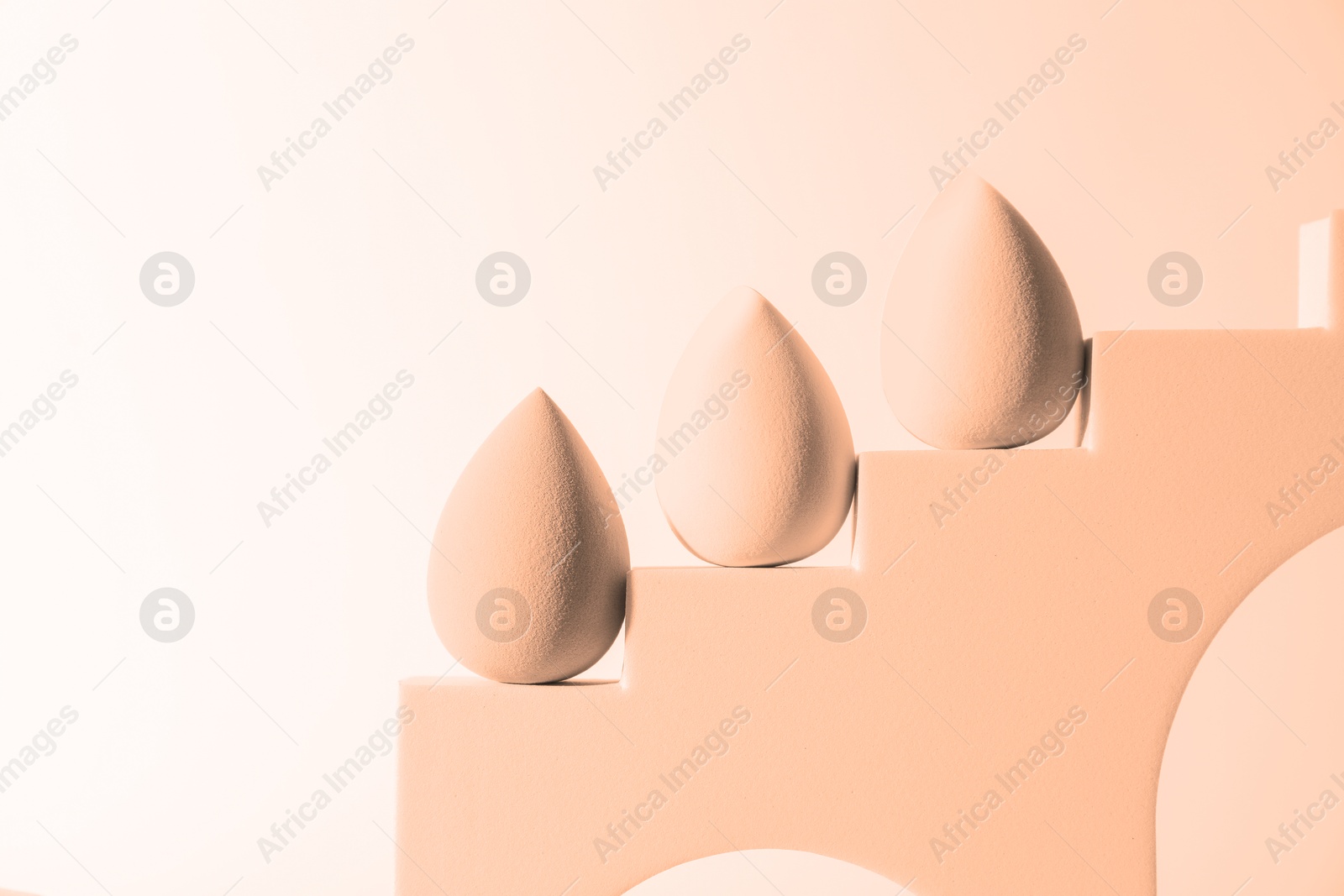 Image of Stylish presentation of makeup sponges on white background, toned in peach fuzz color