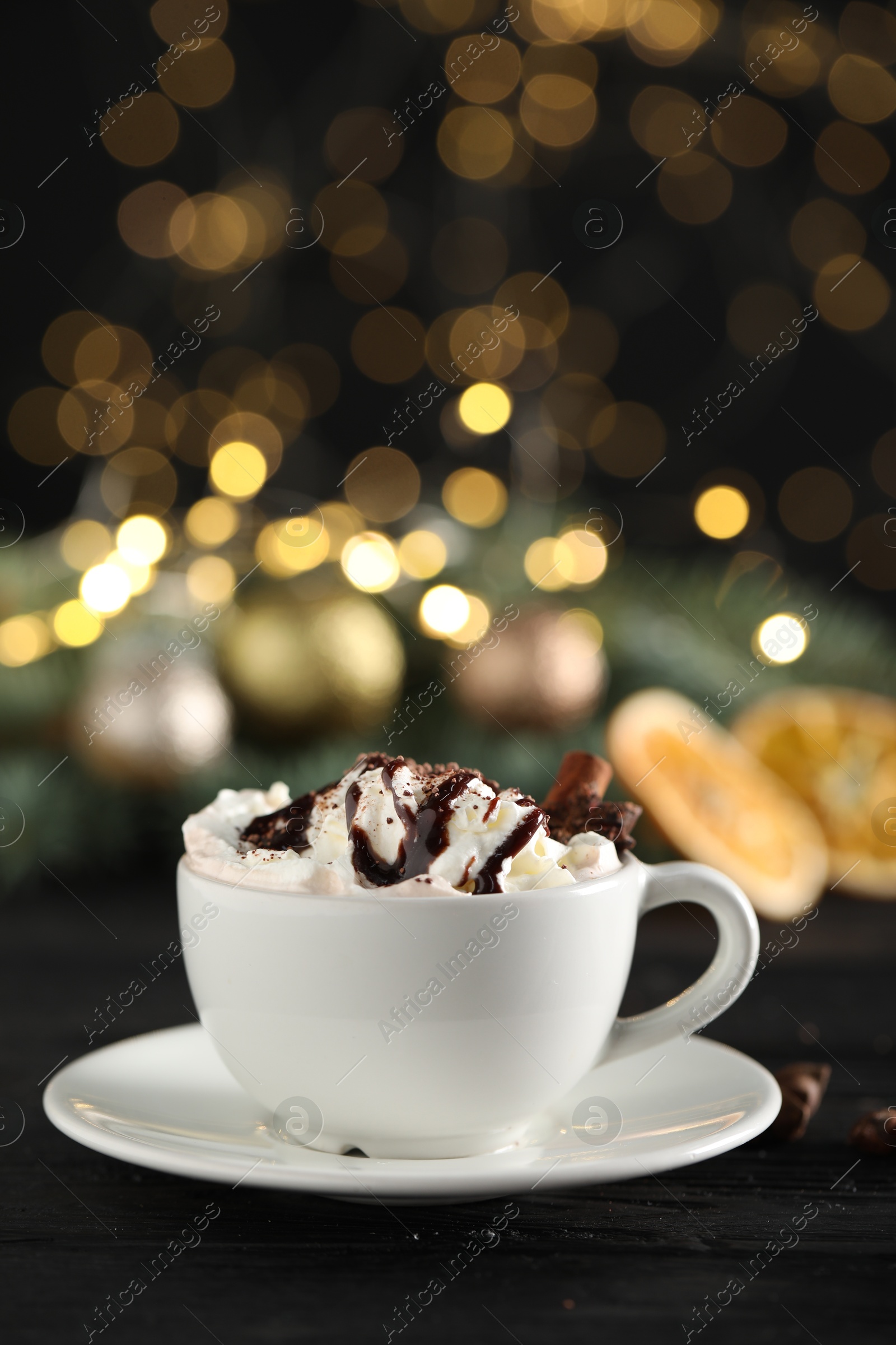 Photo of Tasty hot cocoa drink with whipped cream in cup and spices on black wooden table