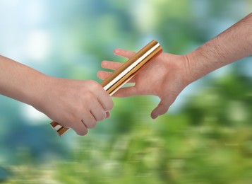 Image of Man passing relay baton to teammate outdoors, closeup