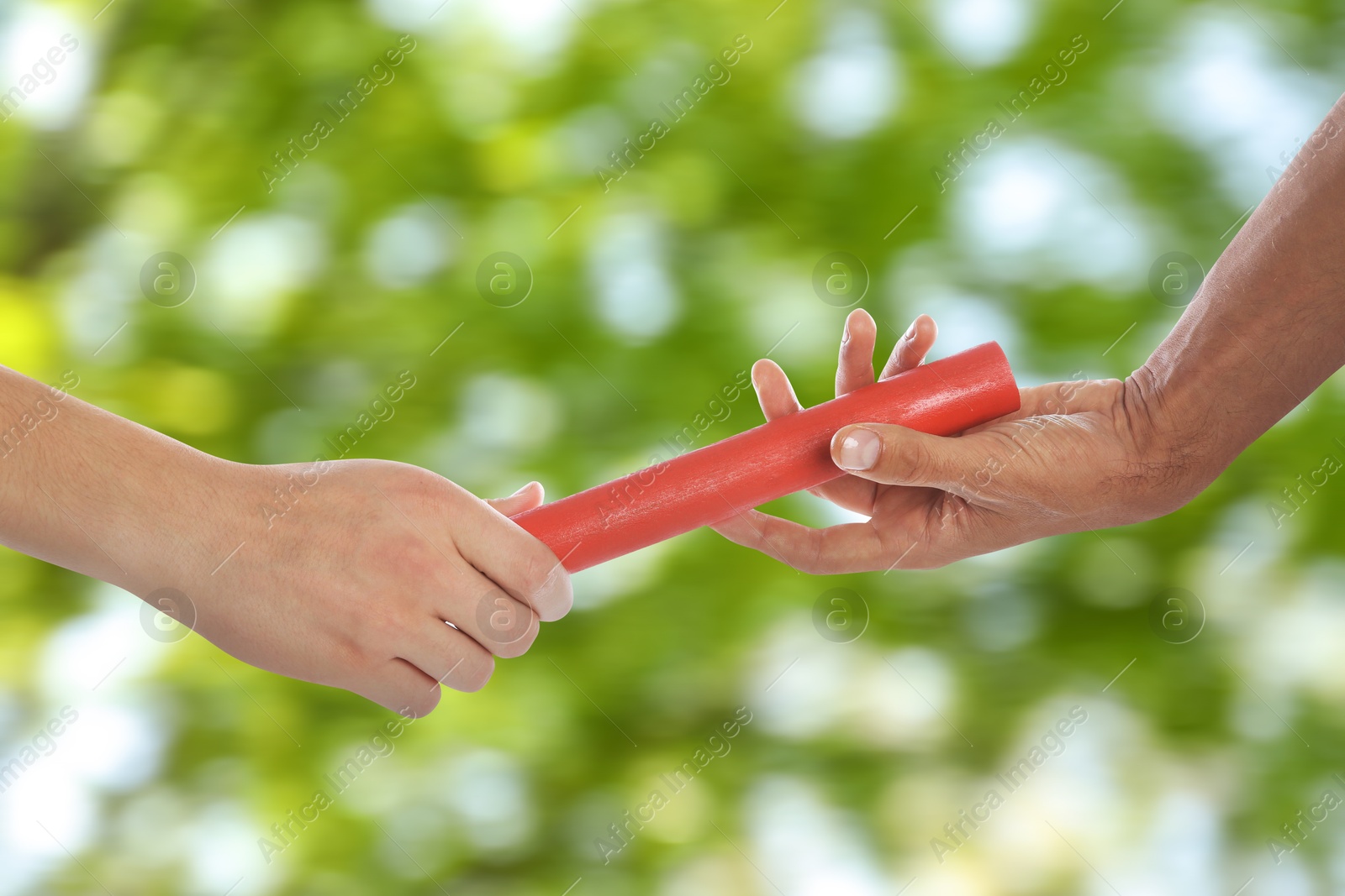 Image of Man passing relay baton to teammate outdoors, closeup