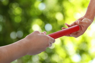 Image of Man passing relay baton to teammate outdoors, closeup