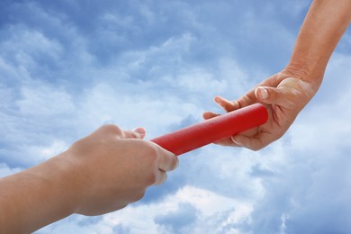 Image of Man passing relay baton to teammate outdoors, closeup