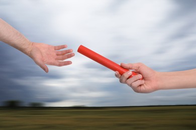 Image of Woman passing baton to man outdoors, closeup