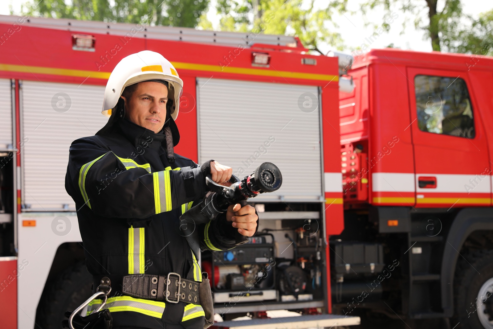 Photo of Firefighter in uniform with high pressure water jet near fire truck outdoors