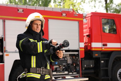 Firefighter in uniform with high pressure water jet near fire truck outdoors