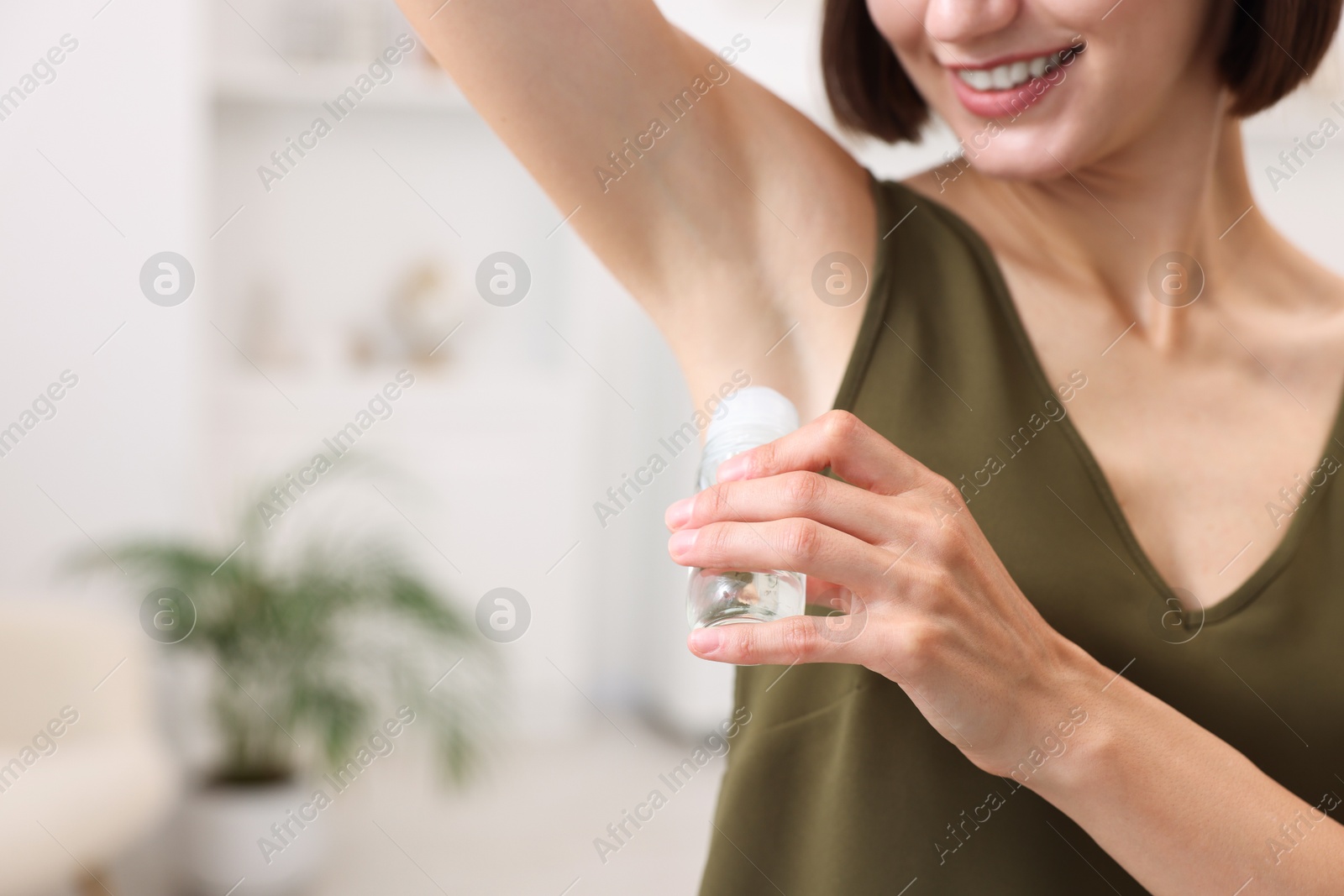 Photo of Smiling woman applying roll-on deodorant at home, closeup. Space for text