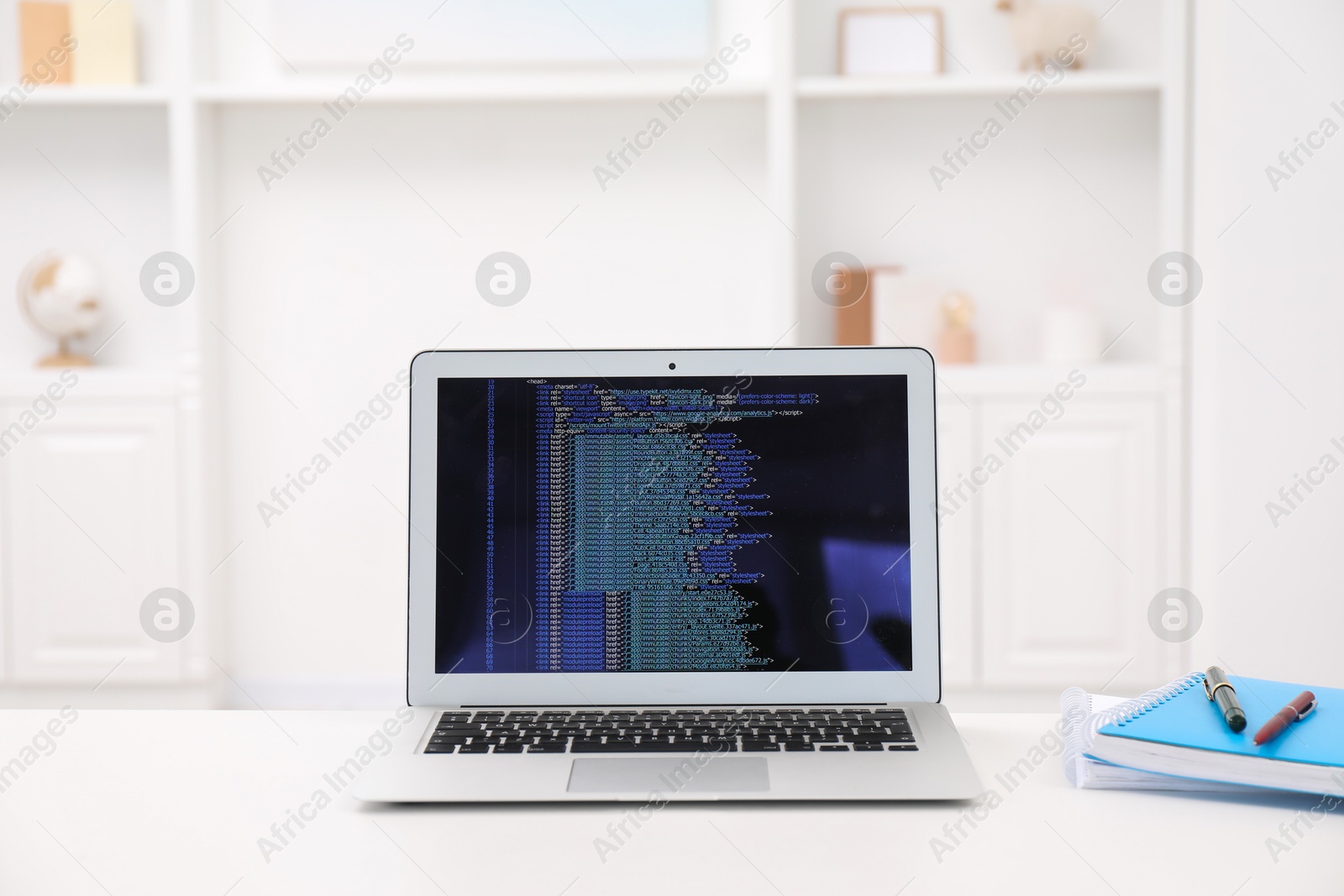 Photo of Programmer's workplace. Modern laptop with unfinished code, notebooks and pens on white desk indoors