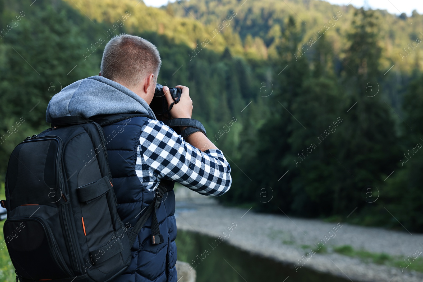 Photo of Photographer with backpack and camera taking picture of beautiful mountains, back view. Space for text