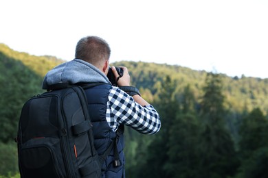 Photographer with backpack and camera taking picture of beautiful mountains, back view. Space for text