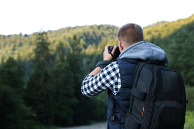 Photographer with backpack and camera taking picture of beautiful mountains, back view. Space for text