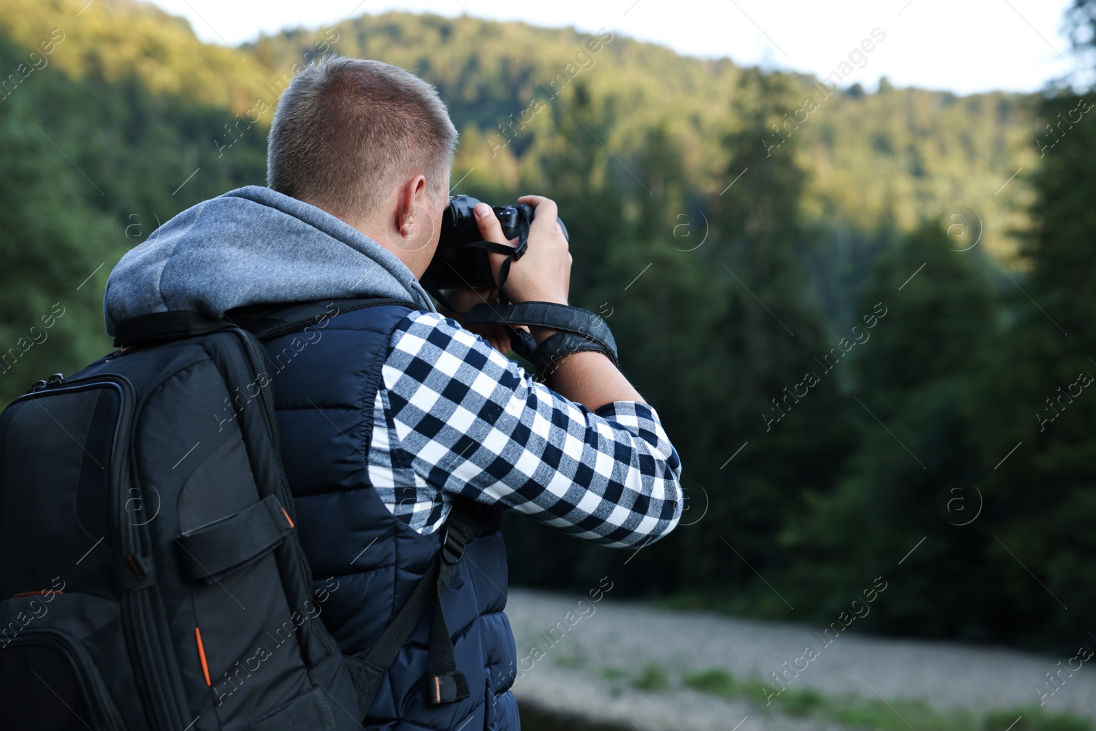 Photo of Photographer with backpack and camera taking picture of beautiful mountains, back view