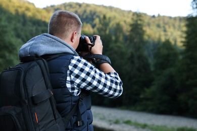 Photographer with backpack and camera taking picture of beautiful mountains, back view