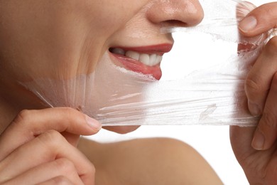 Smiling woman peeling off face mask on white background, closeup