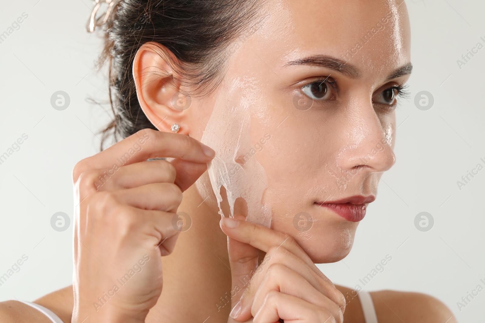 Photo of Beautiful woman peeling off face mask on light grey background, closeup