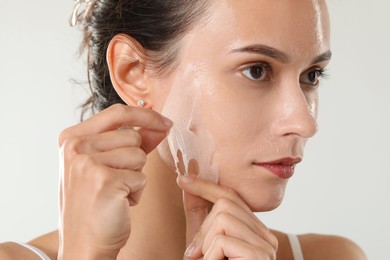 Beautiful woman peeling off face mask on light grey background, closeup