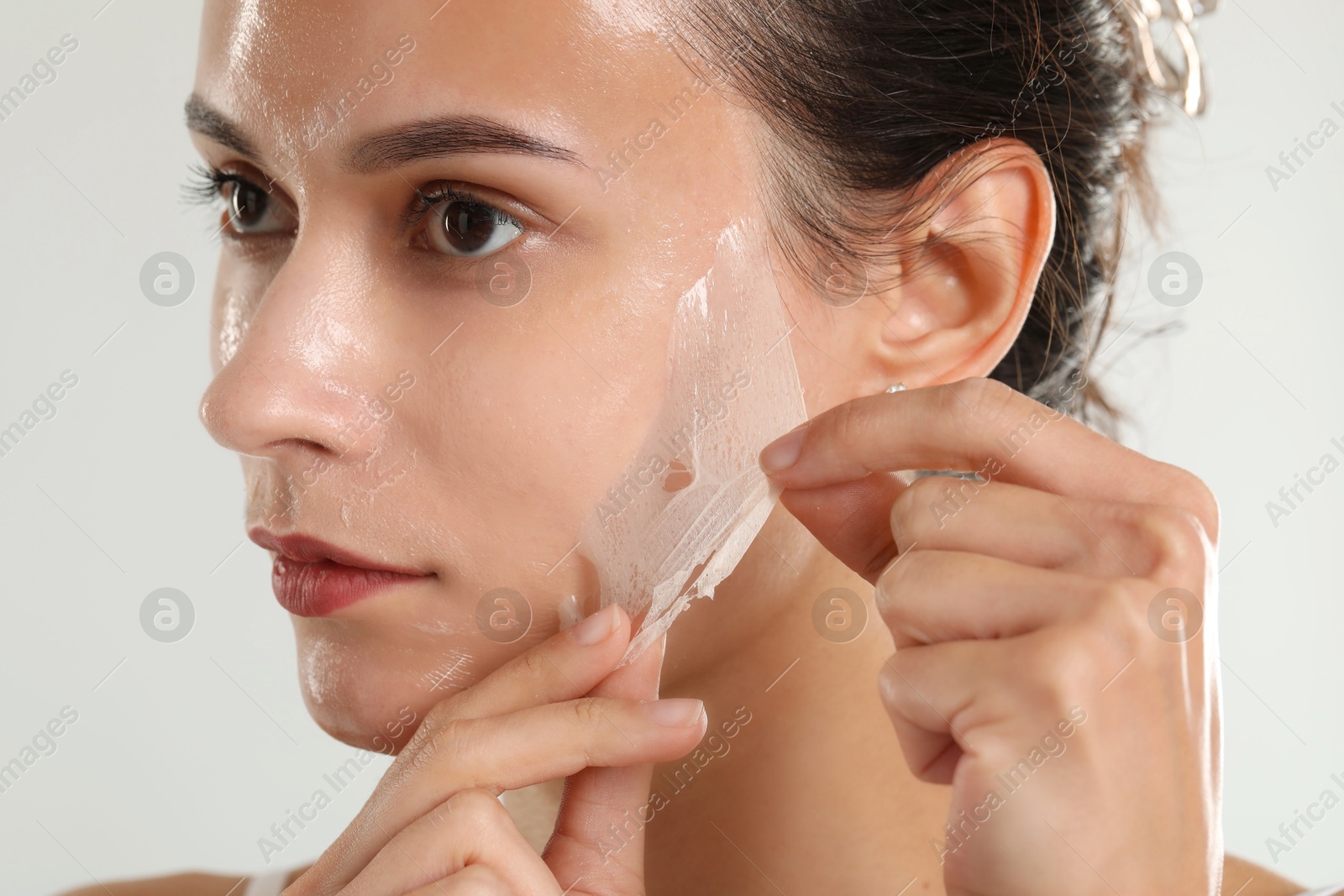 Photo of Beautiful woman peeling off face mask on light grey background, closeup