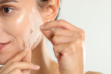 Woman peeling off face mask on light grey background, closeup