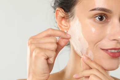 Woman peeling off face mask on light grey background, closeup